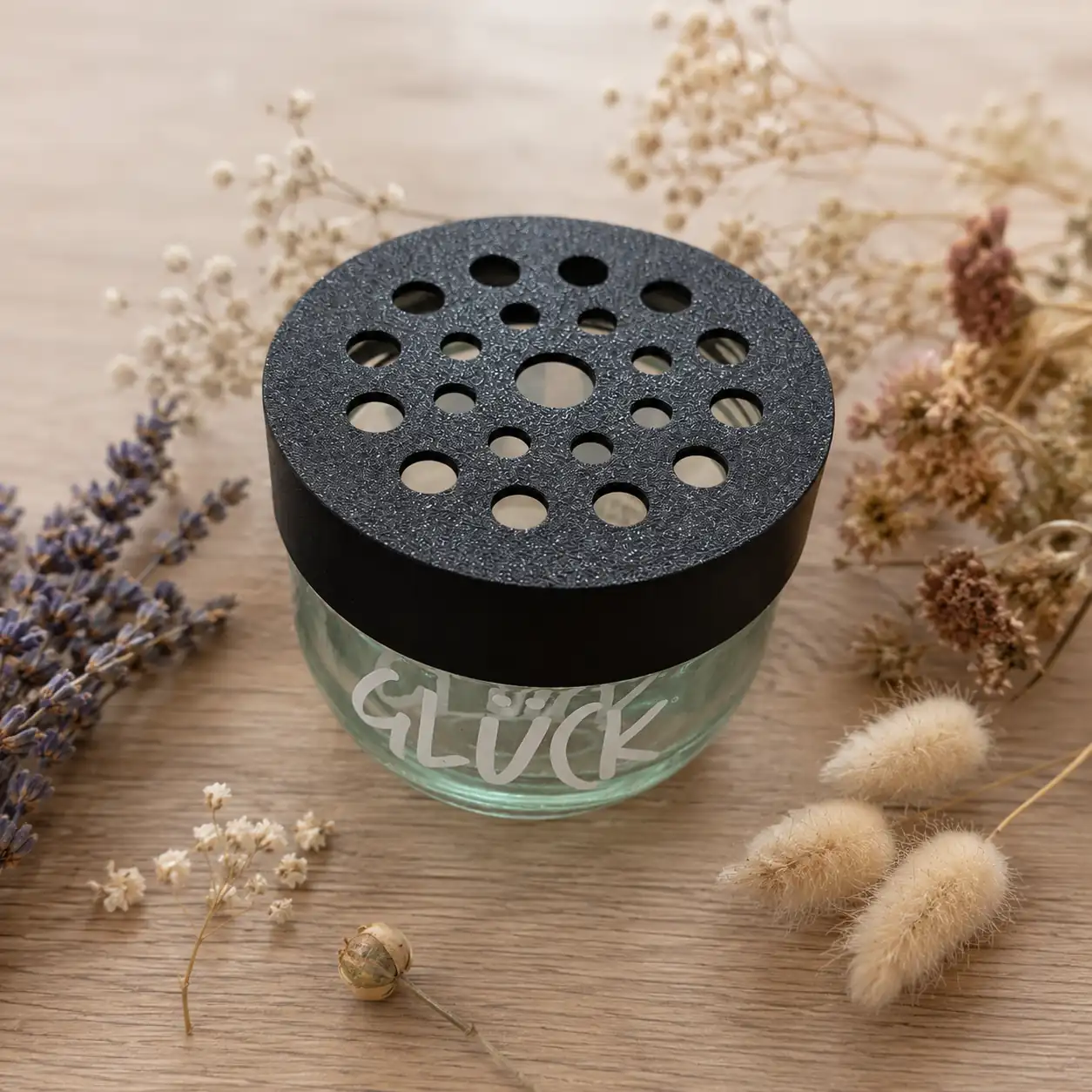 Blumenretter für das Glück Marmeladenglas Kleine Stiche Blumenretter mit Lochmuster auf einem Glücksglas, dekoriert mit Trockenblumen auf einem Holztisch.
